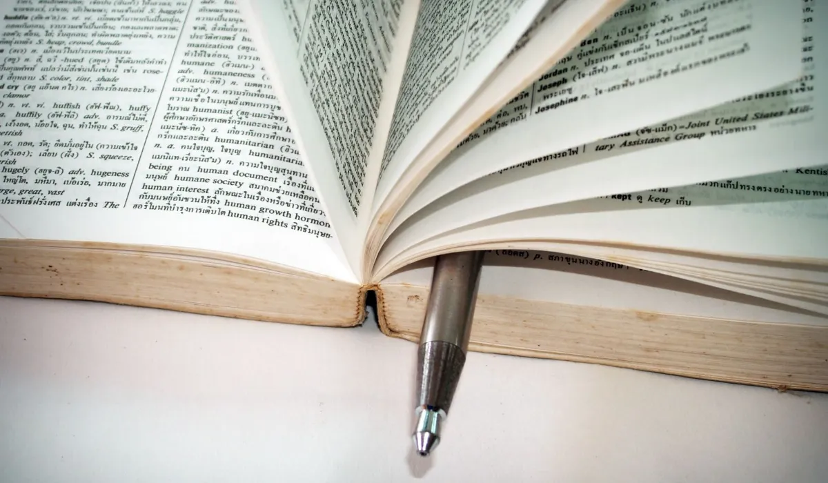 An open bilingual dictionary on a desk with a pen